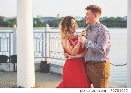 Happy beautiful woman in red dress and young man dance of on summer with lake in the background. Color contrast red and white 70701055