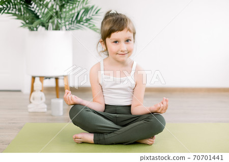 Little Caucasian kid girl wearing sportswear, meditating in a lotus pose with mudra gesture, sitting on green mat, at cozy yoga studio or home. Children doing yoga Little Caucasian kid girl wearing sportswear, meditating in a lotus pose with mudra gesture, sitting on green mat, at cozy yoga studio or home. Children doing yoga 70701441