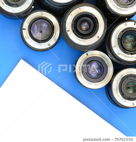Several photographic lenses and white notebook lie on a bright blue background. Space for text Several photographic lenses and white notebook lie on a bright blue background. Space for text 70701550