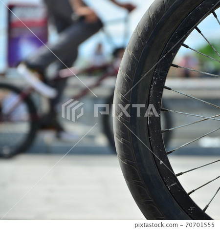 A BMX bike wheel against the backdrop of a blurred street with cycling riders A BMX bike wheel against the backdrop of a blurred street with cycling riders 70701555