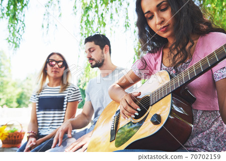 Group of happy friends with guitar. While one of them is playing guitar and others are giving him a round of applause Group of happy friends with guitar. While one of them is playing guitar and others are giving him a round of applause 70702159