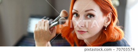 Beautiful redhead woman holding new makeup brushes Beautiful redhead woman holding new makeup brushes 70703574