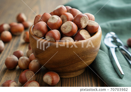 Wooden bowl of hazelnuts and nutcracker on table. Wooden bowl of hazelnuts and nutcracker on table. 70703982