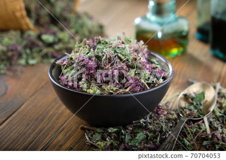 Bowl of dry Origanum vulgare or wild marjoram flowers. Bottle of essential oil on table. 70704053