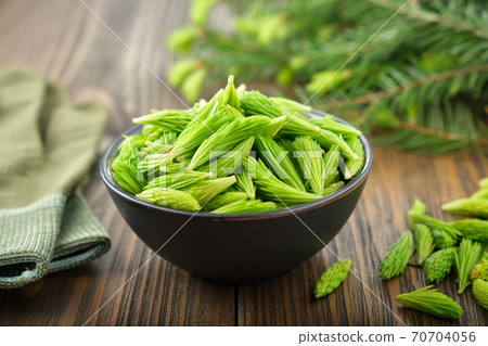 Spruce tips in a black bowl. Fir buds and needles, twigs of fir tree on wooden table. Spruce tips in a black bowl. Fir buds and needles, twigs of fir tree on wooden table. 70704056
