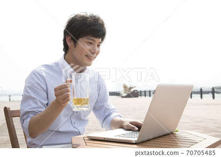 A man who uses a computer while drinking beer 70705485