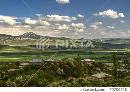 Village in the distance and Azhdahak mountain range on the background of spring blue sky with Cumulus clouds coming from the mountains in Armenia Village in the distance and Azhdahak mountain range on the background of spring blue sky with Cumulus clouds coming from the mountains in Armenia 70706538