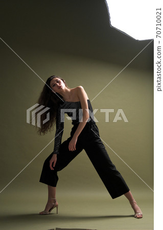 A beautiful young tall girl with long black hair poses in a shiny blouse and black culottes on a green background. Buty and fashion photo shoot. A beautiful young tall girl with long black hair poses in a shiny blouse and black culottes on a green background. Buty and fashion photo shoot. 70710021