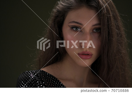 A beautiful young tall girl with long black hair poses in a shiny blouse and black culottes on a green background. Buty and fashion photo shoot. A beautiful young tall girl with long black hair poses in a shiny blouse and black culottes on a green background. Buty and fashion photo shoot. 70710886