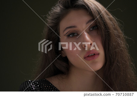 A beautiful young tall girl with long black hair poses in a shiny blouse and black culottes on a green background. Buty and fashion photo shoot. A beautiful young tall girl with long black hair poses in a shiny blouse and black culottes on a green background. Buty and fashion photo shoot. 70710887