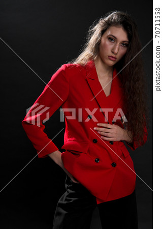 A young beautiful oriental woman with long black hair in a red jacket against a black background. The fashion model poses in the studio. 70711558