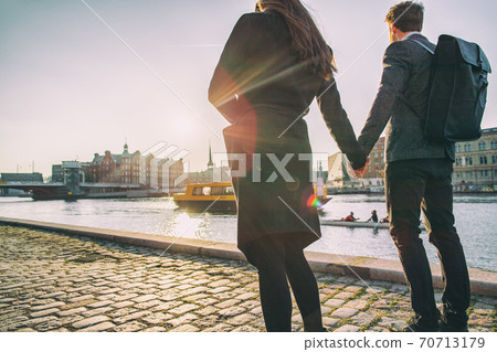 Couple walking on city street at sunset wearing elegant professional coats for fall or autumn. Copenhagen harbour lifestyle young people on outdoor stroll 70713179