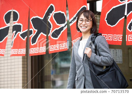 A smiling young woman coming out of a ramen shop alone 70713570