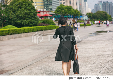 Business woman lady walking away on Shanghai city street wearing elegant silk shirtdress for professional work realtor. Mature businesswoman commute in China Business woman lady walking away on Shanghai city street wearing elegant silk shirtdress for professional work realtor. Mature businesswoman commute in China 70714539