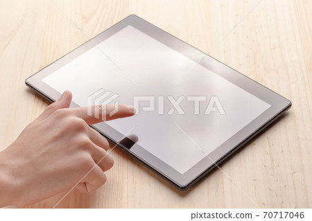 Hands use a black tablet on a wooden table, sunlit from the window Hands use a black tablet on a wooden table, sunlit from the window 70717046