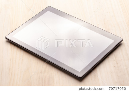 Black digital tablet on a wooden table under the light from the window 70717050