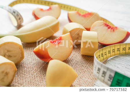 Slices of banana and peach spread out on a sack on a black wooden table with a centimeter. Diet breakfast and body control Slices of banana and peach spread out on a sack on a black wooden table with a centimeter. Diet breakfast and body control 70717382