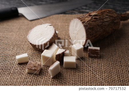Sliced yucca root on a sackcloth on a black wooden table with a knife. Tropical food ingredients Sliced yucca root on a sackcloth on a black wooden table with a knife. Tropical food ingredients 70717532