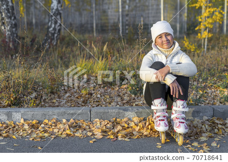 Young caucasian girl in roller blades resting sitting on concrete curb. Space for text. Young caucasian girl in roller blades resting sitting on concrete curb. Space for text. 70718641