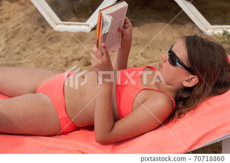 A girl in a pink swimsuit lies on a sun lounger and reads a book 70718860