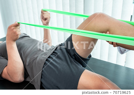 Female Physiotherapist working examining treating injured leg of patient, Doing exercises the Rehabilitation therapy pain his in clinic Female Physiotherapist working examining treating injured leg of patient, Doing exercises the Rehabilitation therapy pain his in clinic 70719625