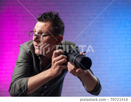 crazy man in glasses with a digital camera on a bright neon background crazy man in glasses with a digital camera on a bright neon background 70721418