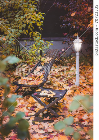 Street lamp and garden wooden chairs on autumn leaves background Street lamp and garden wooden chairs on autumn leaves background 70723335