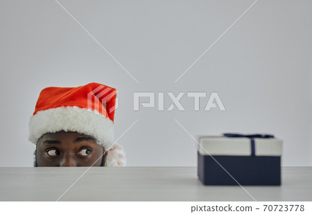 The african man in the santa hat watching from the table with a gift 70723778