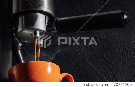 Espresso pouring from coffee machine into orange cup. 70725709