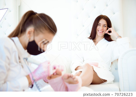 Pedicurist's hands in protective rubber gloves applying nail polish to the toenails Pedicurist's hands in protective rubber gloves applying nail polish to the toenails 70726223