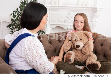 Teen girl on reception at the psychotherapist. Psychotherapy session for children. The psychologist works with the patient. Girl smiling sitting on a sofa next to a sitting female doctor therapist 70726484