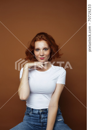 young pretty redhead girl posing cheerful on warm brown background, lifestyle people concept 70729233