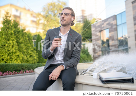 Male office worker enjoying coffee near fountain 70730001