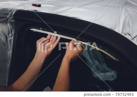 Mechanic preparing a car for painting by protecting the edges. Mechanic preparing a car for painting by protecting the edges. 70732403