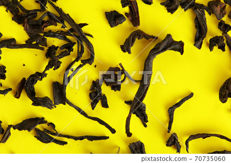 Dry black loose tea leaves on yellow board, closeup detail from above Dry black loose tea leaves on yellow board, closeup detail from above 70735060