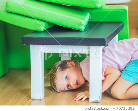 Cute little freckled face blond boy artistic facial expressions gestures, mischievous in good mood have fun at amusement playground entertainment center, hiding under the table. Happy childhood 70735398