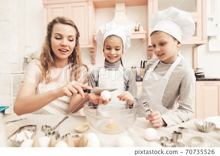 Mom helps daughter break eggs into the dishes. Mom helps daughter break eggs into the dishes. 70735526
