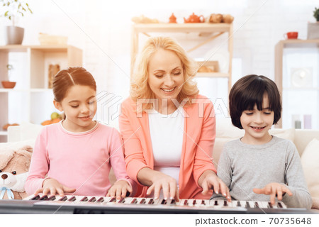 Woman teaches grandchildren to play synthesizer. Woman teaches grandchildren to play synthesizer. 70735648