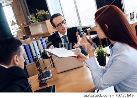 A lawyer in a suit gives the couple a document. A lawyer in a suit gives the couple a document. 70735649