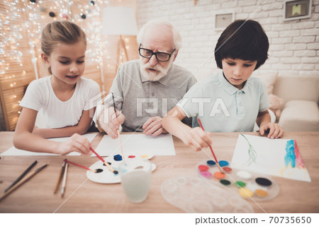 Grandfather sits with his grandchildren at table. Grandfather sits with his grandchildren at table. 70735650