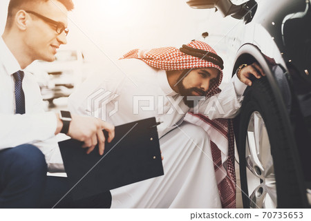 Arab man looks under the wheel of a car. Arab man looks under the wheel of a car. 70735653