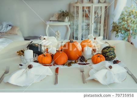 Festive table setting for Thanksgiving family home dinner. Fall composition with decorative pumpkins, nuts, cones, fallen leaves, and candles in light interior. Natural autumn decor. Selective focus Festive table setting for Thanksgiving family home dinner. Fall composition with decorative pumpkins, nuts, cones, fallen leaves, and candles in light interior. Natural autumn decor. Selective focus 70735958