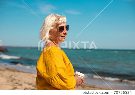Adult woman with coffee to go by the sea on a sunny day Adult woman with coffee to go by the sea on a sunny day 70736524