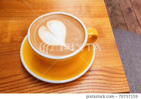 Yellow cup of coffee with heart shaped latte art 70737159