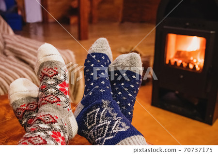 Feet in wool socks warming near fireplace in rustic cabin house. Cozy winter. Feet in wool socks warming near fireplace in rustic cabin house. Cozy winter. 70737175