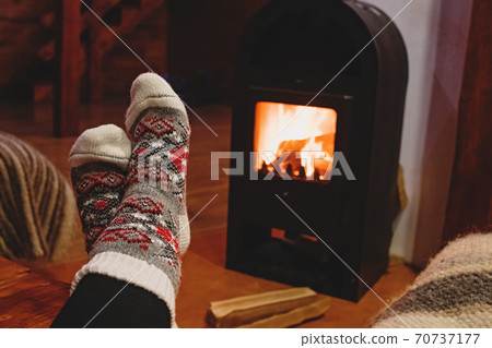 Feet in wool socks warming near fireplace in rustic cabin house. Cozy winter. Feet in wool socks warming near fireplace in rustic cabin house. Cozy winter. 70737177