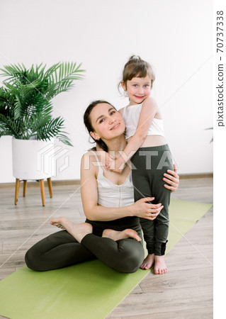 Mother and daughter spending time together doing yoga exercise at yoga studio. Pretty woman and little child girl, hugging each other after joint fitness training, mom sits in lotus pose. Family sport Mother and daughter spending time together doing yoga exercise at yoga studio. Pretty woman and little child girl, hugging each other after joint fitness training, mom sits in lotus pose. Family sport 70737338