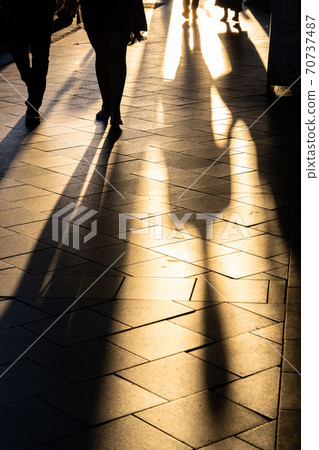 Long human shadows projected on the pavement at sunset 70737487