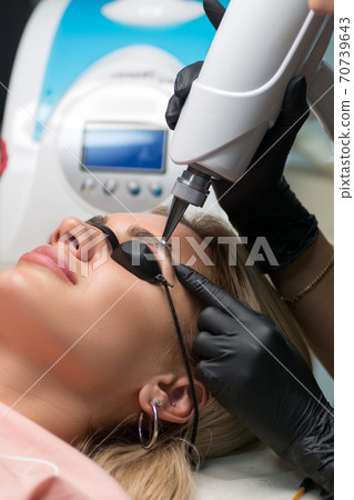 Laser removal of permanent makeup. The beautician removes the tattoo from the eyebrows. 70739643