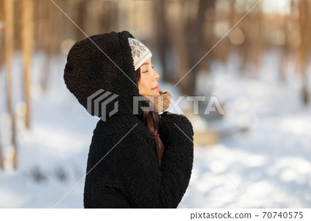 Winter happy woman relaxing breathing cold air outside young people lifestyle. Asian girl with closed eyes breathing wellness and health in forest wearing hooded jacket and hat 70740575